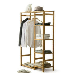 Bamboo open wardrobe clothes rack with a jacket and shirts on the rail and folded clothes, books and slippers on shelves