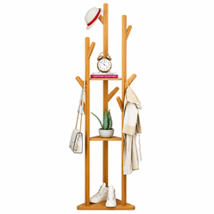 Bamboo tree coat rack with branch hooks and two small shelves holding a hat, handbag, coat, clock, plant and sneakers