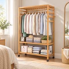 Bamboo clothes rack with shirts on hangers and folded clothes, books and storage boxes on the shelves in a bright bedroom