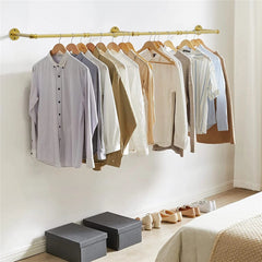 Gold wall mounted pipe clothes rack with shirts on wooden hangers above shoe boxes and shoes in a bedroom