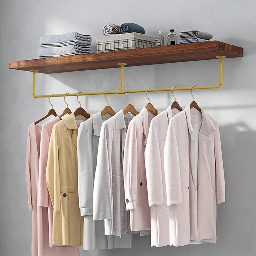 Gold pipe clothes rail mounted under a wooden shelf with coats on wooden hangers and towels on the shelf