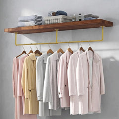 Gold pipe clothes rail mounted under a wooden shelf with coats on wooden hangers and towels on the shelf