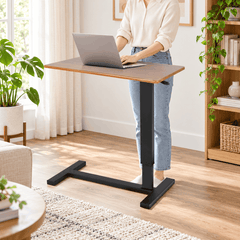 Person using a laptop at a raised height adjustable table with a wood look top and black base in a bright living room
