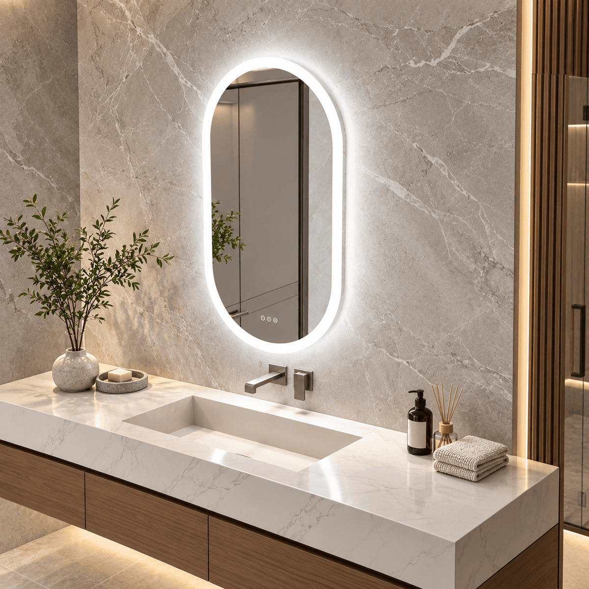 Angled view of an oval LED mirror with a bright white glowing edge above a marble vanity, plant and towels