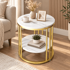Round gold bar frame side table with two white marble look tops beside a sofa holding a cup, a vase, a frame and a plant