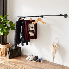 Black wall mounted pipe clothes rail in a hallway with a sweater, jacket and shirt on hangers above a duffel bag and sneakers